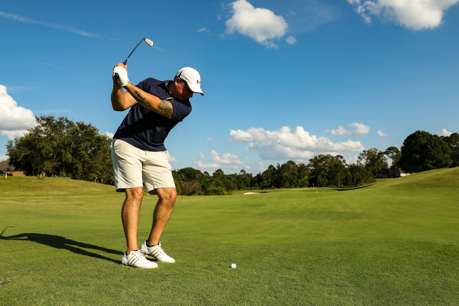 Photo by Mick Haupt man in black shirt and white shorts playing golf during daytime